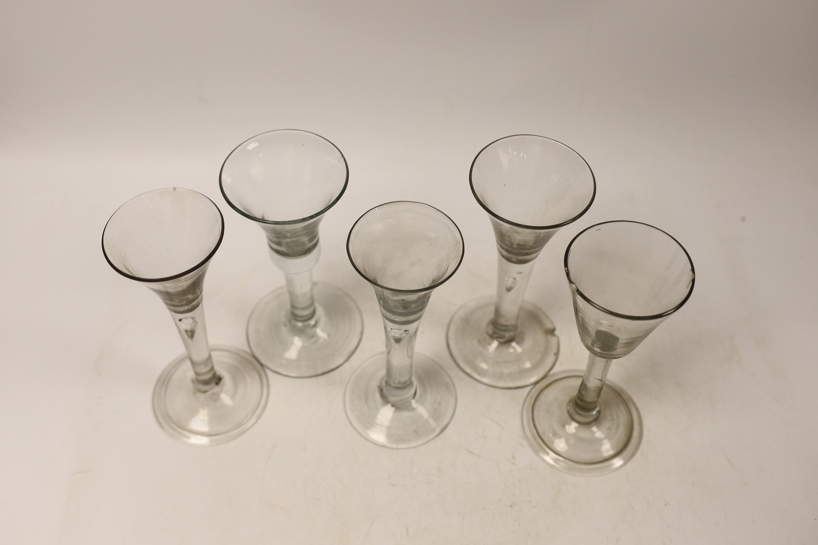 Five mid-18th century plain stem wine glasses, including three with drawn trumpet shaped bowls, two examples with folded feet, tallest 16cm